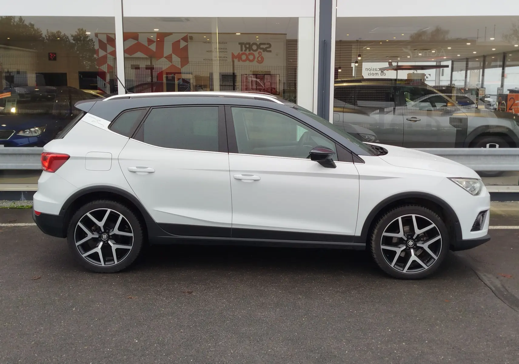 Vue de profil côté gauche d'un SEAT Arona blanc avec toit gris magnétique et jantes alliage noires et argentées.
