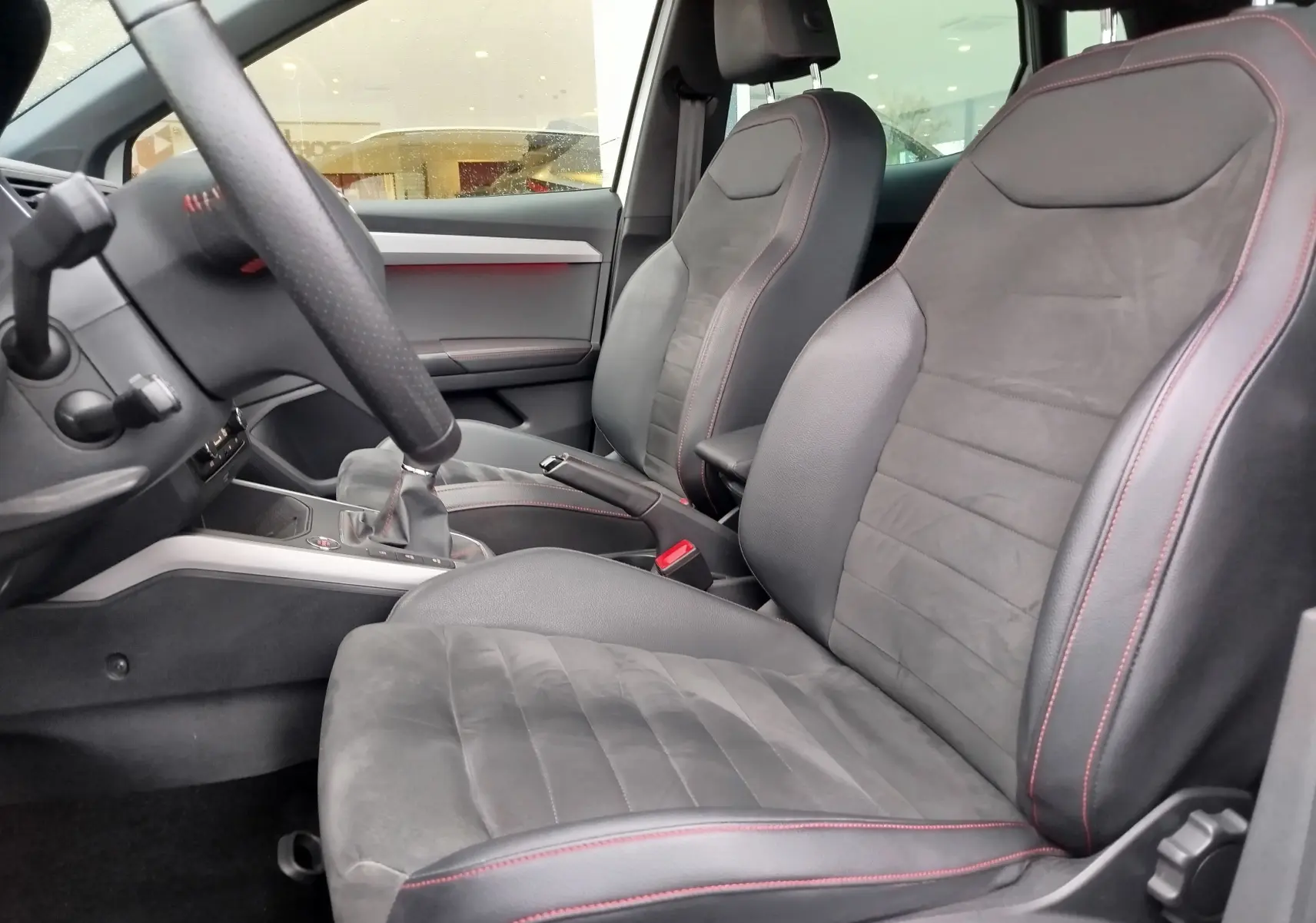Vue intérieure côté conducteur de la SEAT Arona 2020, sièges en cuir noir avec surpiqûres rouges et volant partiel visible.
