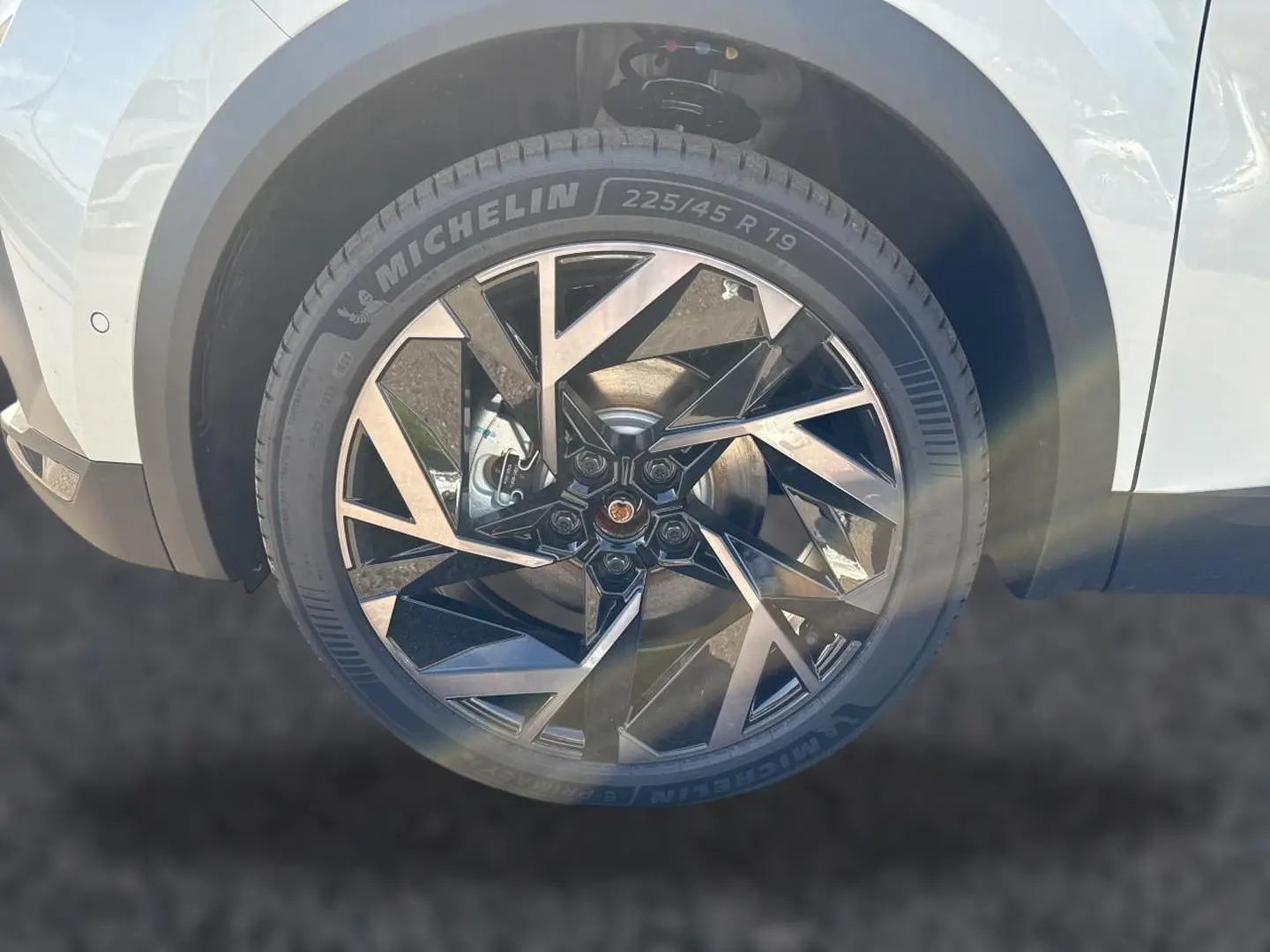 Gros plan sur la roue avant droite blanche nacrée du Renault Symbioz 1.8 e-tech avec jante alu au design géométrique noir et argent.