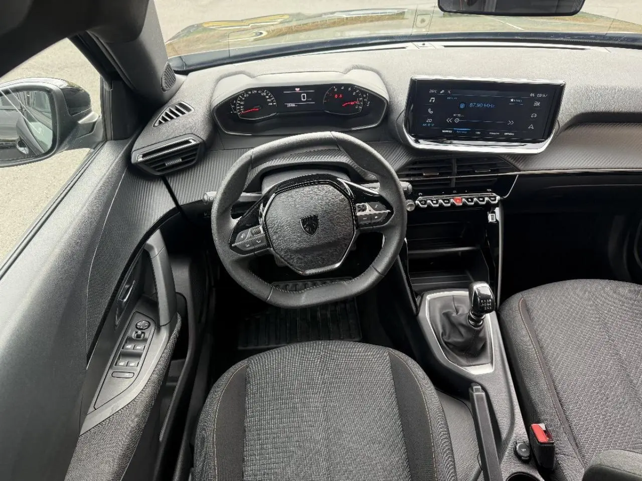 Vue intérieure de face du poste de conduite d'une Peugeot 2008 noire, avec volant compact, tableau de bord numérique et boîte manuelle.