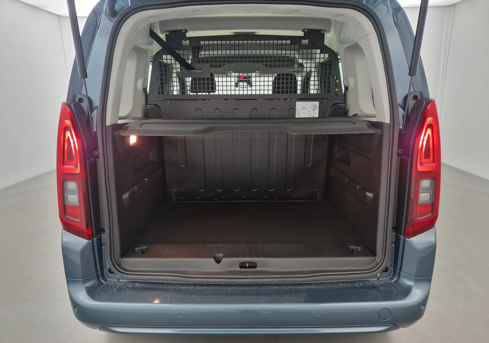 Vue arrière ouverte de l'Opel Combo Life bleu Kiama, montrant le coffre spacieux avec grille de séparation et tablette amovible.