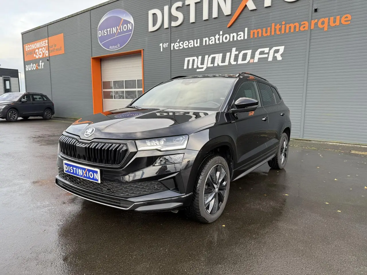 Vue 3/4 avant d'un Skoda Karoq noir Magic nacré avec jantes alliage et calandre noire devant un bâtiment Distinxion.