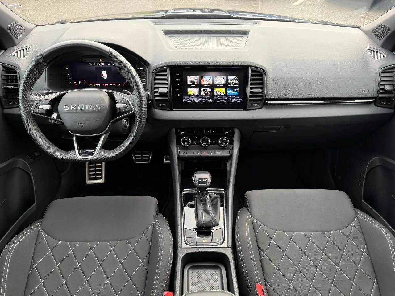 Intérieur noir du Skoda Karoq 2025, vue frontale sur le tableau de bord, volant sport et console centrale avec écran tactile.