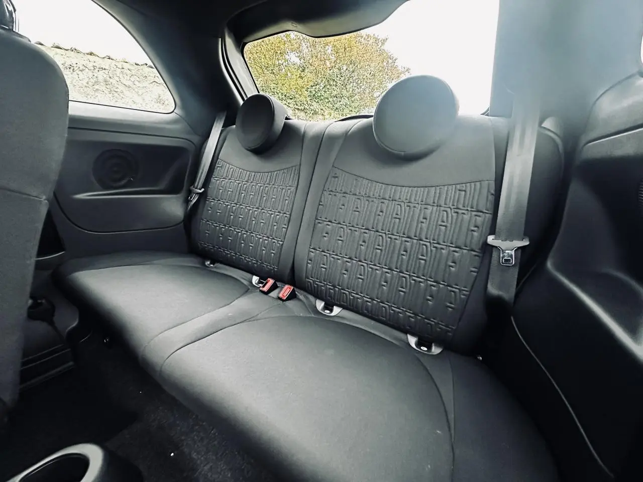 Vue intérieure de la banquette arrière gris foncé de la Fiat 500 2023 avec appuie-têtes ronds et ceintures de sécurité.