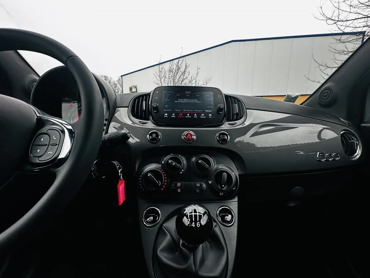 Vue intérieure frontale du tableau de bord gris foncé de la Fiat 500 2023 avec levier de vitesse manuel et écran tactile central.