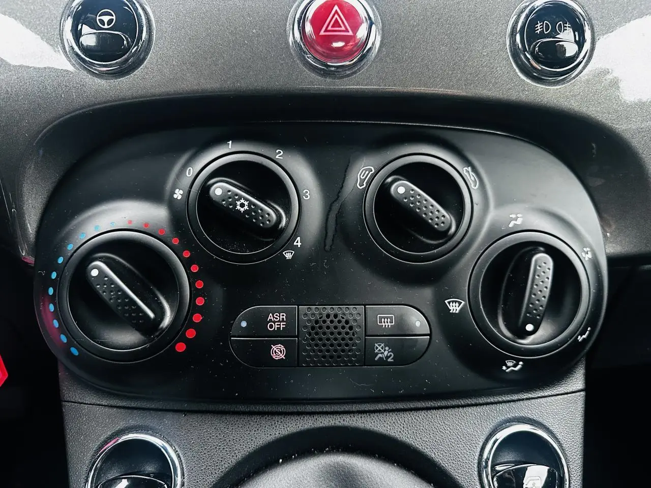 Gros plan sur la console centrale noire de la Fiat 500 gris foncé, montrant les commandes de climatisation et boutons de sécurité.