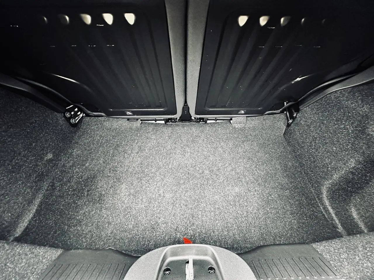 Coffre ouvert vu de face avec banquette arrière rabattue, intérieur gris foncé et tapis de sol gris.