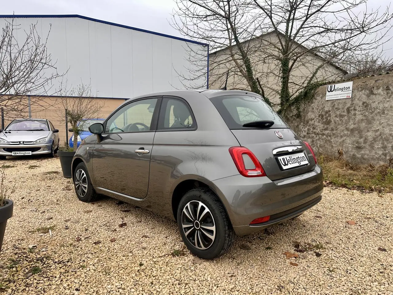 Fiat 500 gris foncé vue 3/4 arrière droit, jantes alliage et poignées chromées visibles.