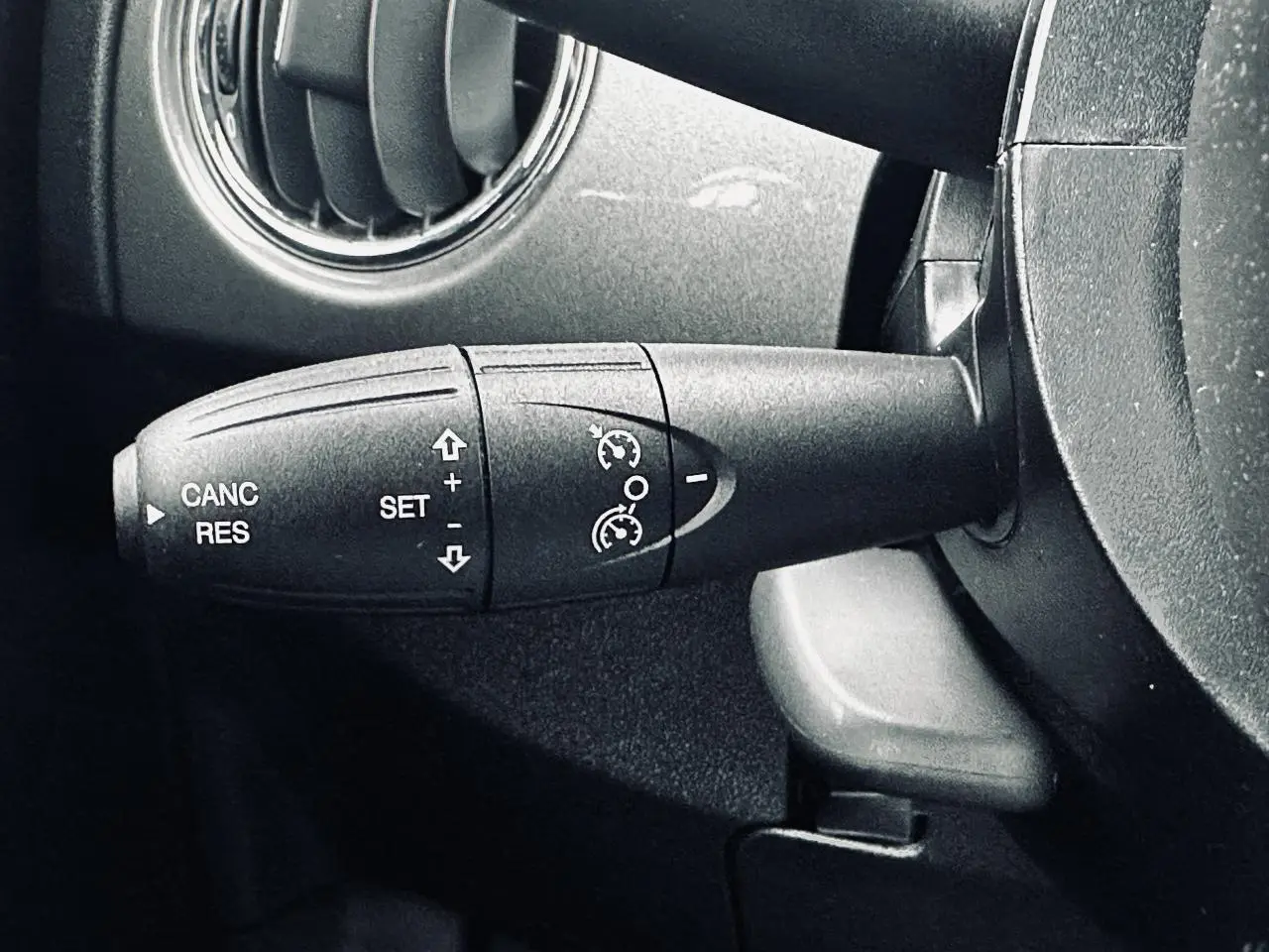 Gros plan sur la commande de régulateur de vitesse à gauche du volant dans l'habitacle gris foncé d'une Fiat 500 2023.