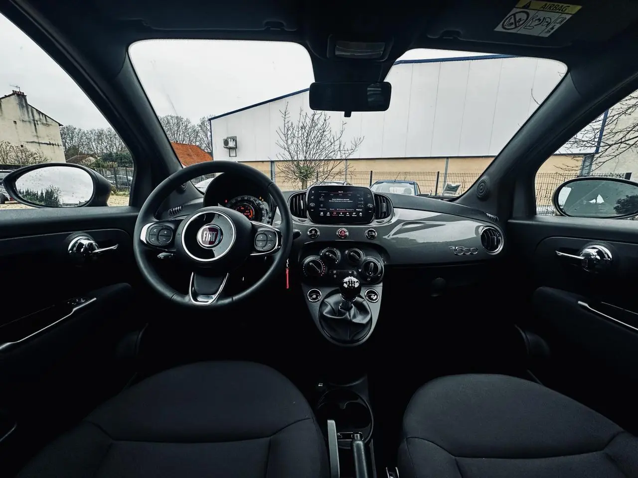 Vue intérieure frontale du tableau de bord gris foncé et volant noir de la Fiat 500 2023 avec boîte manuelle.