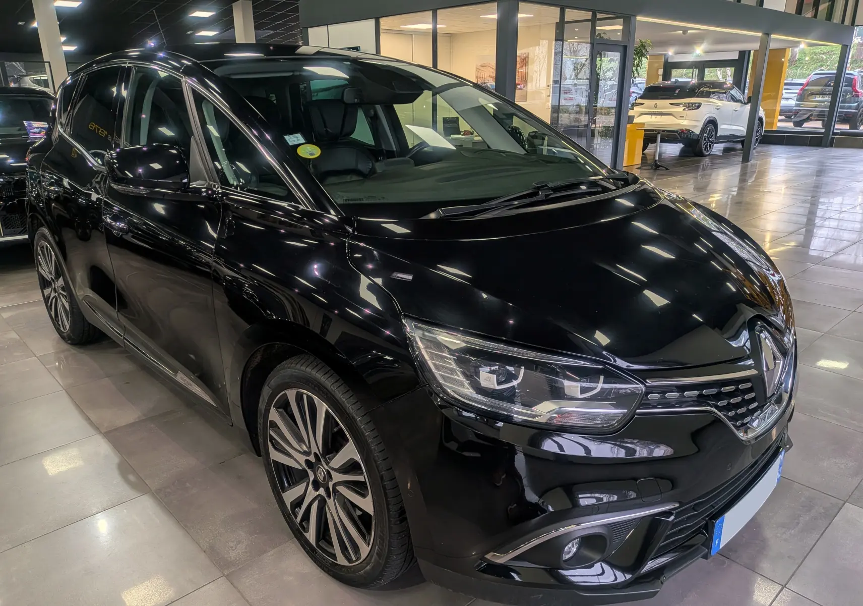 Vue 3/4 avant gauche d’un Renault Scénic IV noir étoilé avec jantes alliage et phares LED dans un showroom.