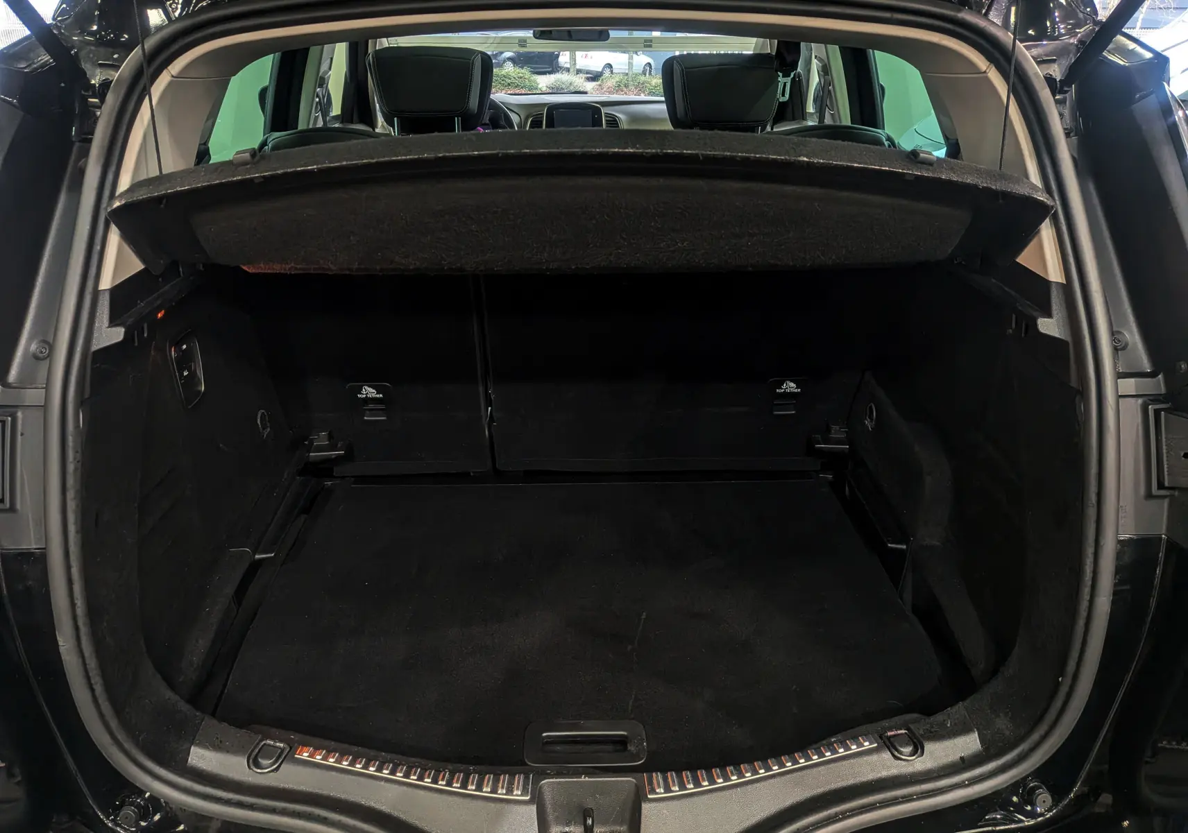 Coffre ouvert vu de l'arrière d'un Renault Scénic IV noir étoilé, montrant l'espace de chargement et la tablette cache-bagages.