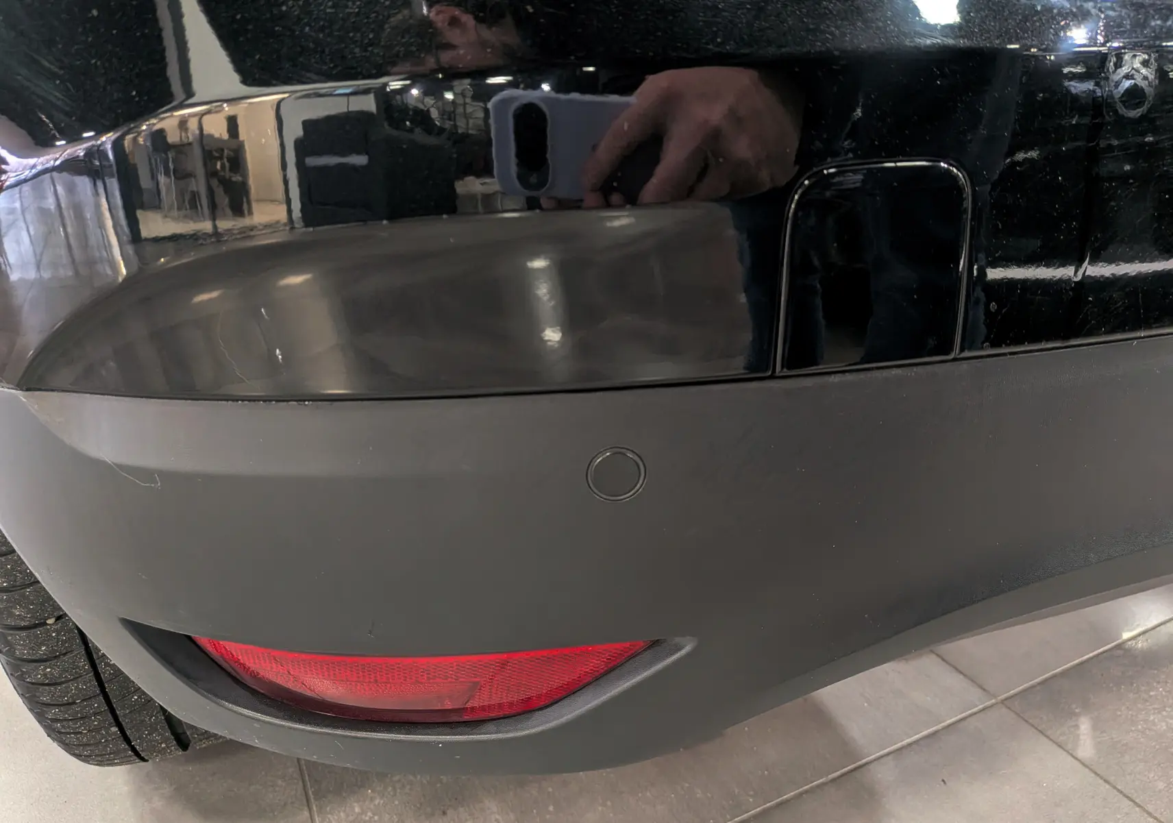 Gros plan sur le pare-chocs arrière noir étoilé du Renault Scénic IV, avec feu antibrouillard et capteur de recul visible.