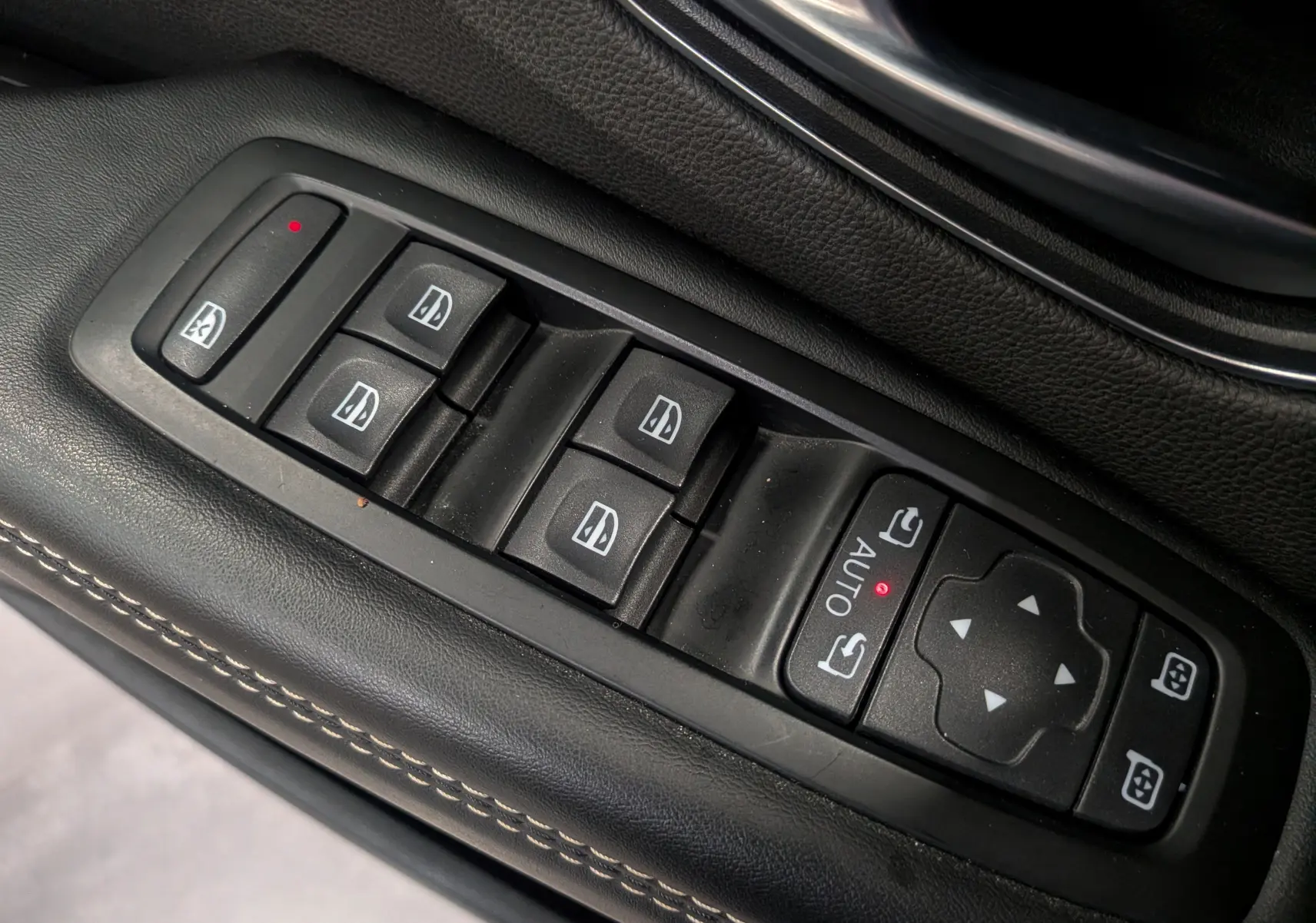 Gros plan sur les commandes de lève-vitres et rétroviseurs électriques sur la porte côté conducteur en cuir noir du Renault Scénic IV.