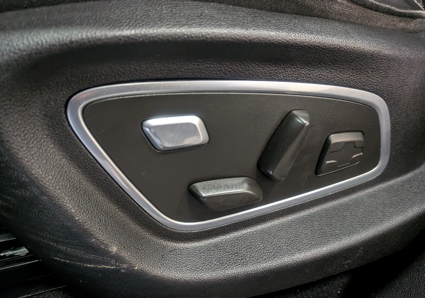 Gros plan sur les commandes de réglage électrique du siège côté conducteur d’un Renault Scénic IV noir étoilé.