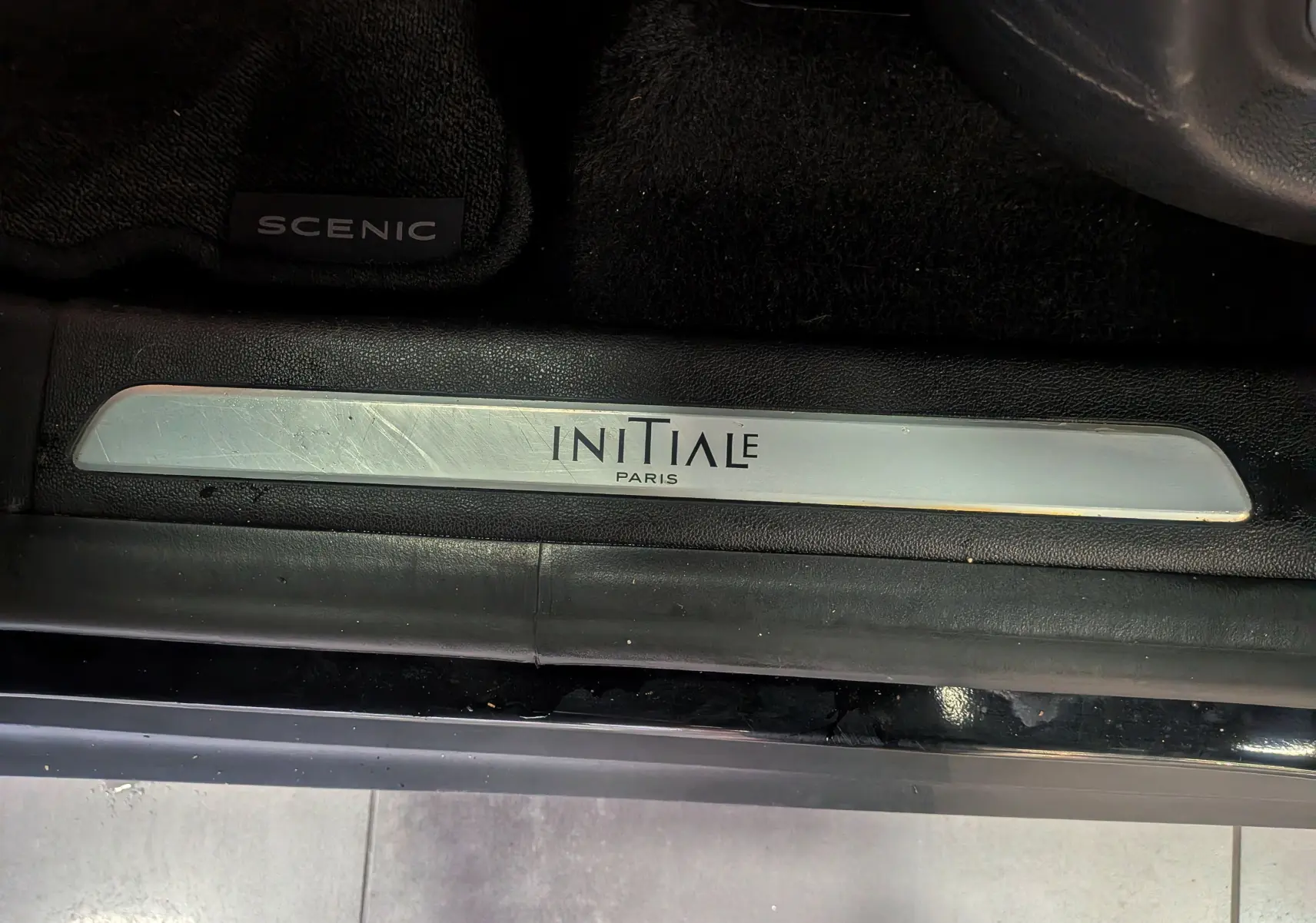 Gros plan sur la plaque de seuil de porte "Initiale Paris" et tapis noir du Renault Scénic IV noir étoilé.