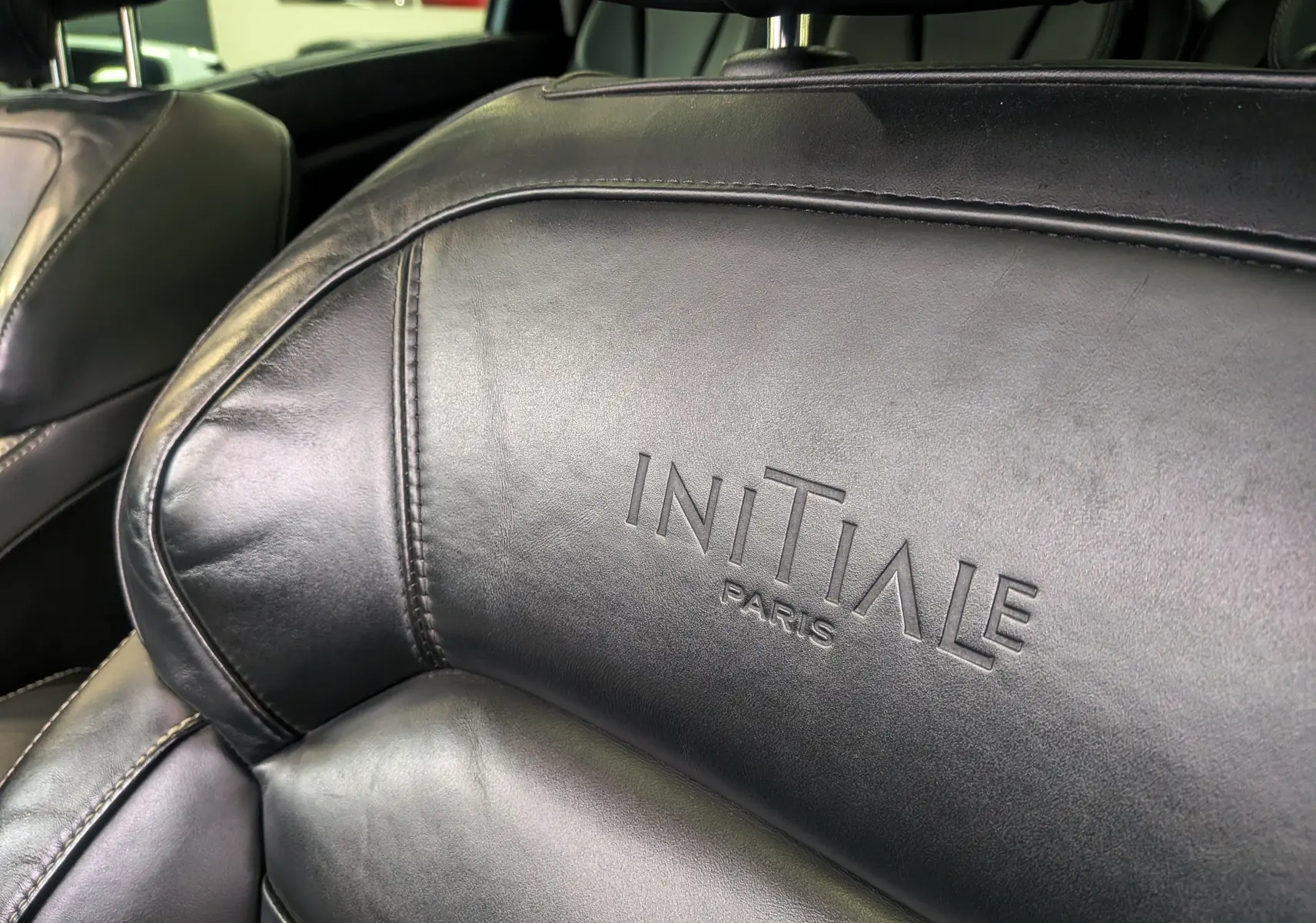 Gros plan sur le cuir noir étoilé du siège avant gauche avec le logo Initiale Paris embossé, intérieur Renault Scenic IV.