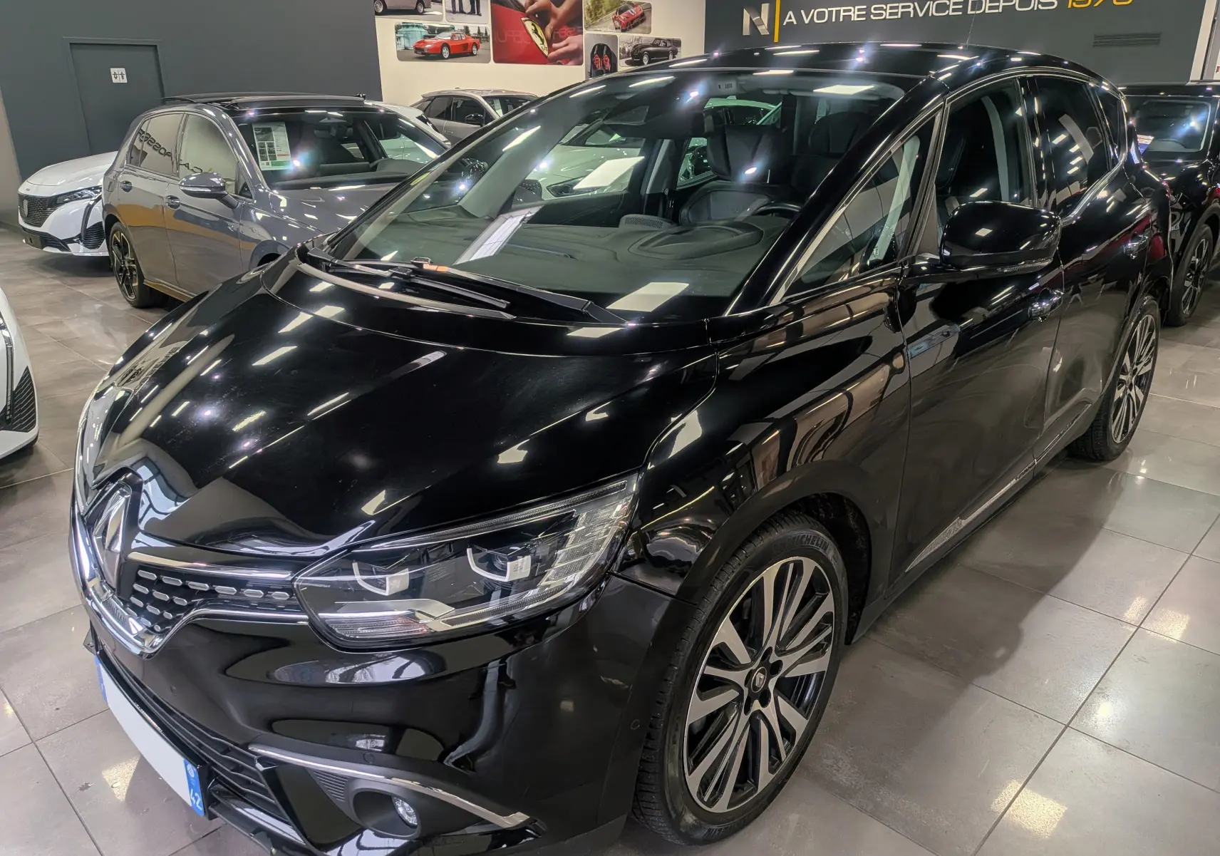 Renault Scénic IV noir étoilé en 3/4 avant droit, avec jantes alliage bi-ton et phares LED visibles en showroom.