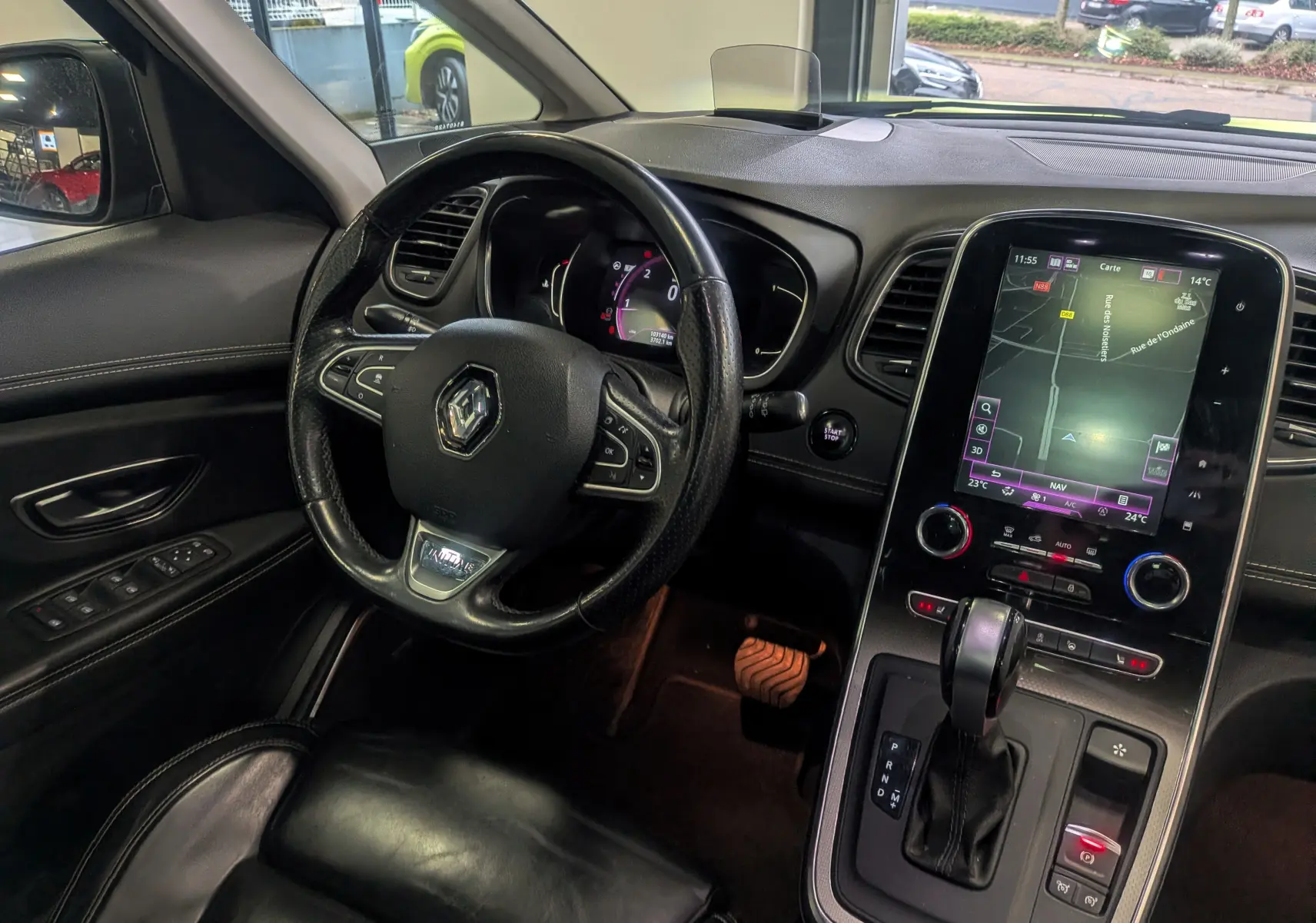 Vue intérieure côté conducteur du Renault Scénic IV noir étoilé, avec volant cuir, écran tactile central et levier de boîte automatique.