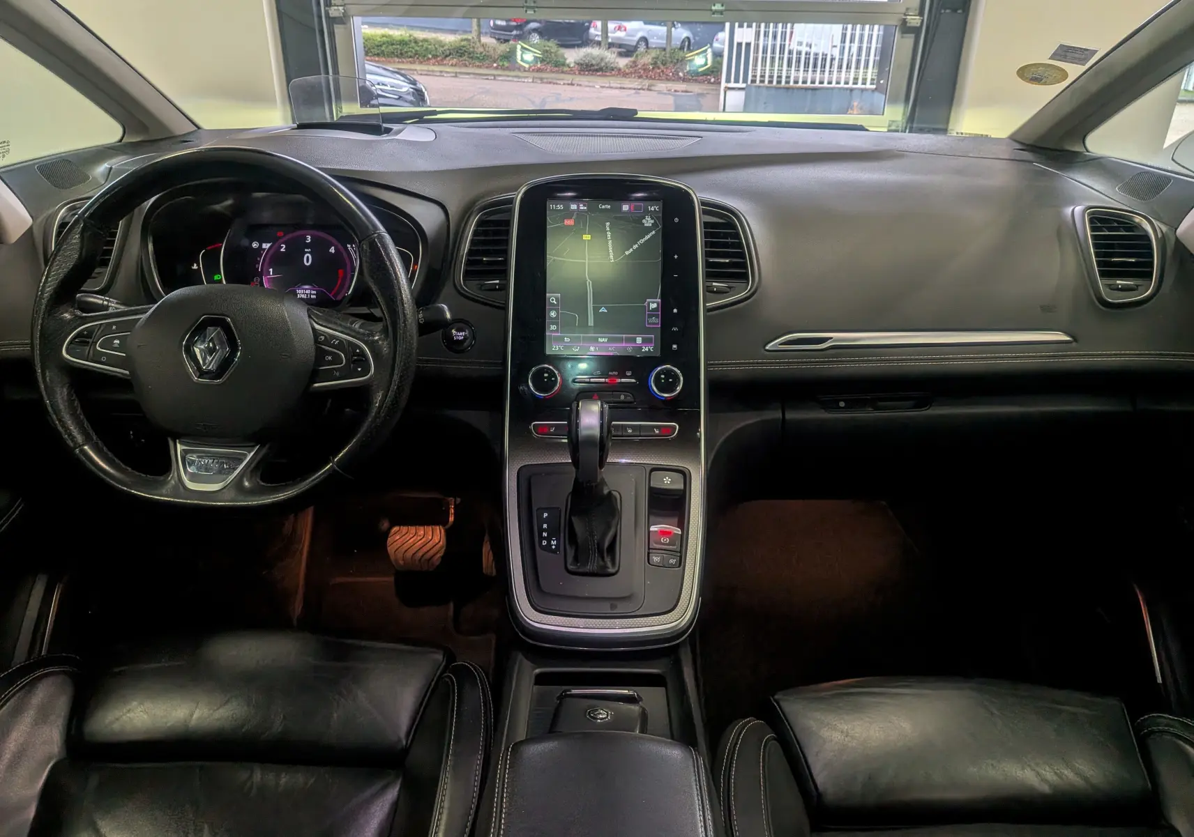 Vue intérieure avant du Renault Scénic IV noir étoilé, mettant en valeur le volant multifonction, l'écran tactile central et la console avec boîte automatique.