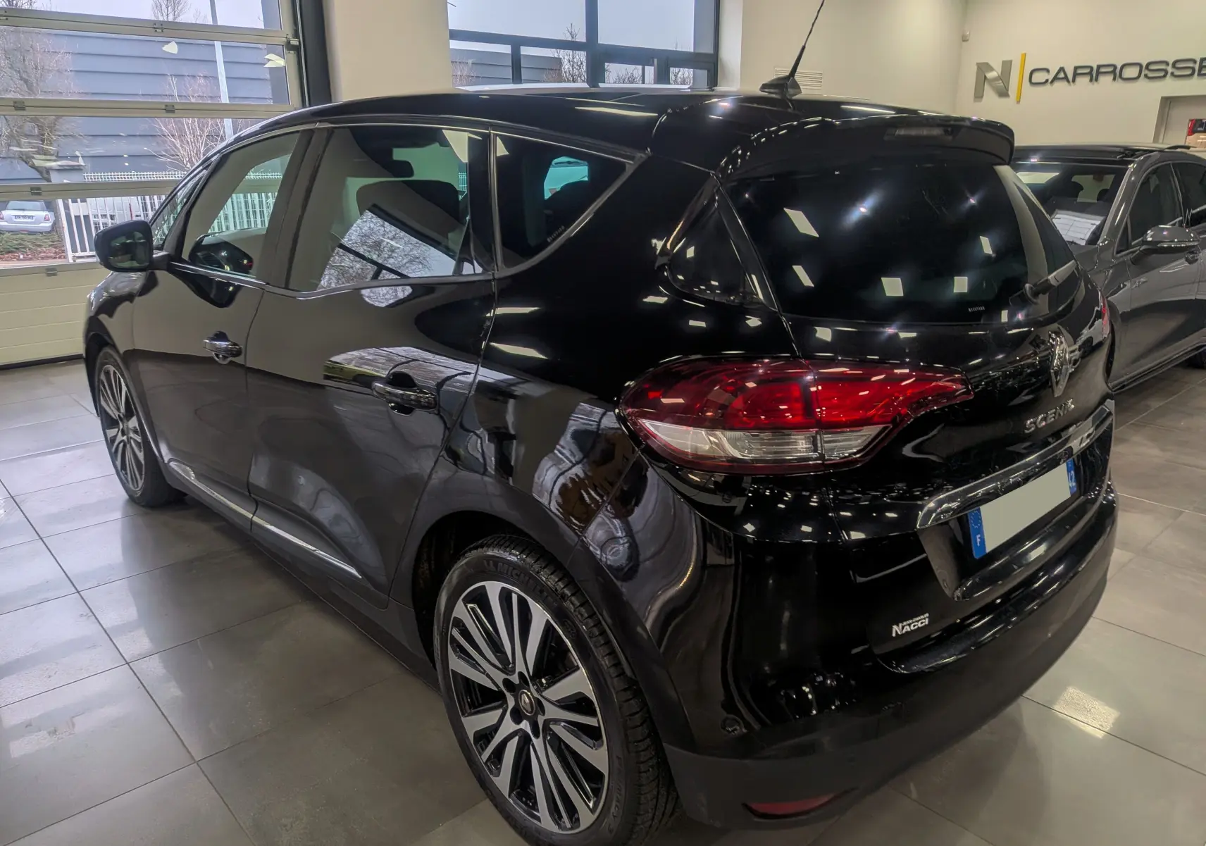 Vue 3/4 arrière droite d’un Renault Scénic IV noir étoilé, mettant en valeur ses feux arrière et jantes bi-ton élégantes.