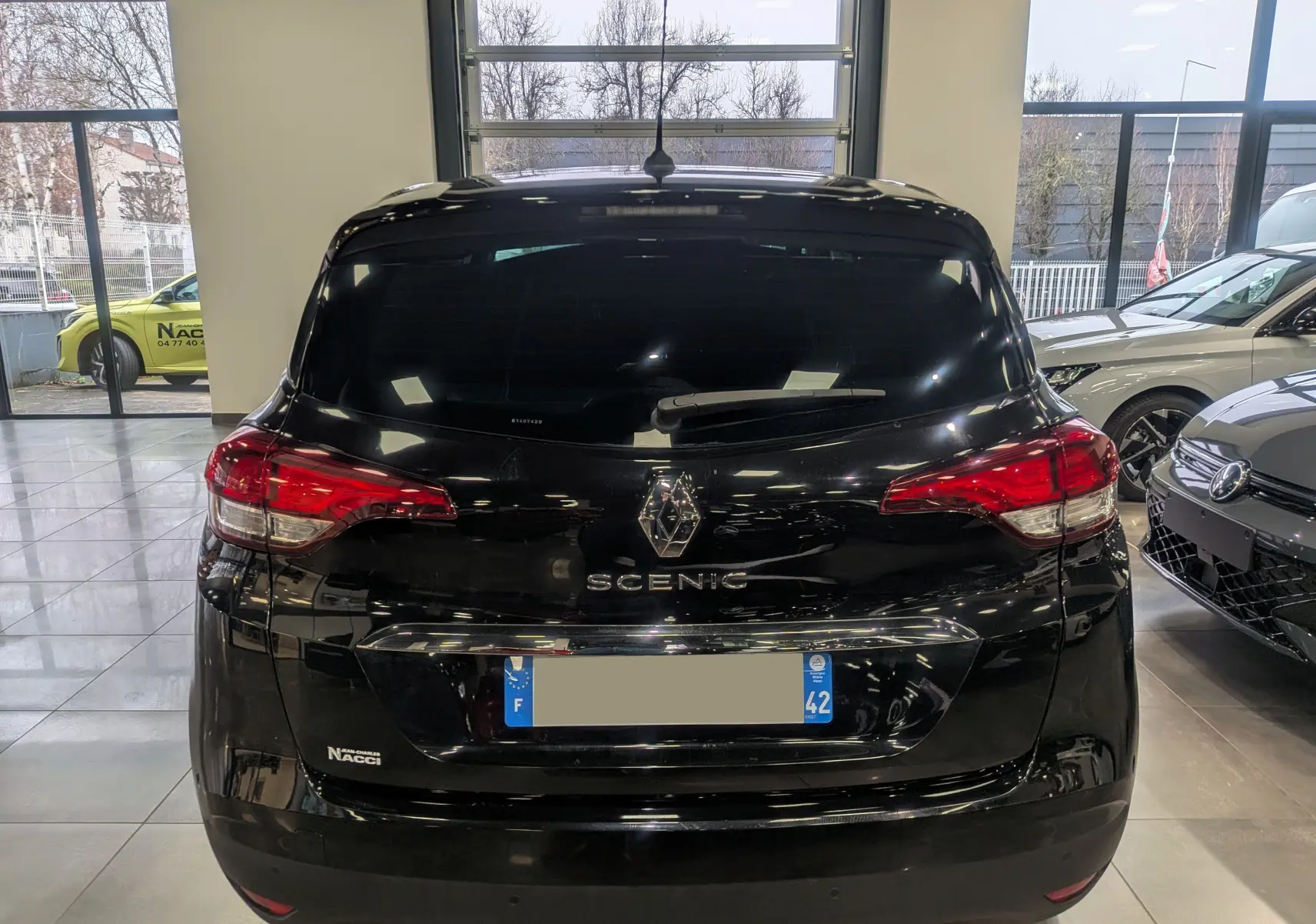 Vue arrière d’un Renault Scénic IV noir étoilé stationné en intérieur avec feux arrière rouges et vitres teintées.
