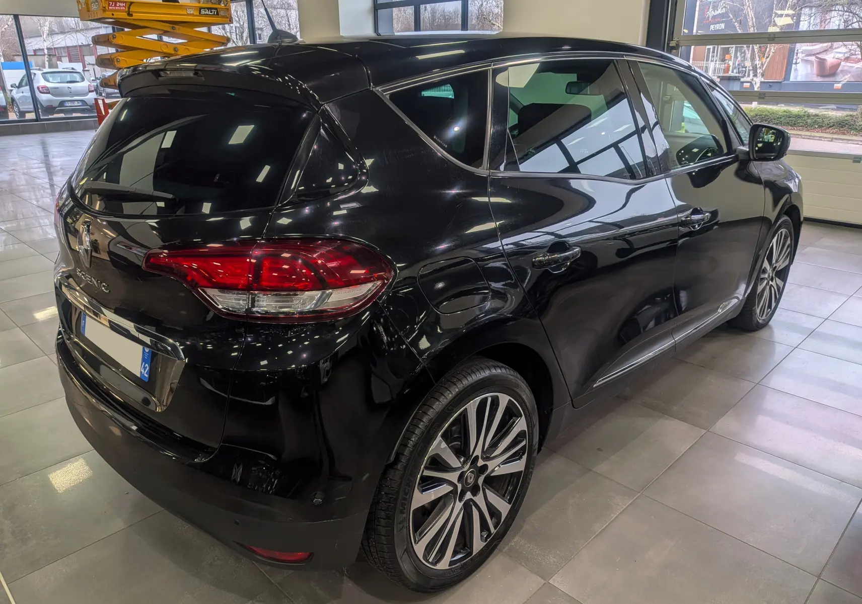 Vue 3/4 arrière droite d'un Renault Scénic IV noir étoilé, avec jantes alliage et vitres teintées en intérieur showroom.