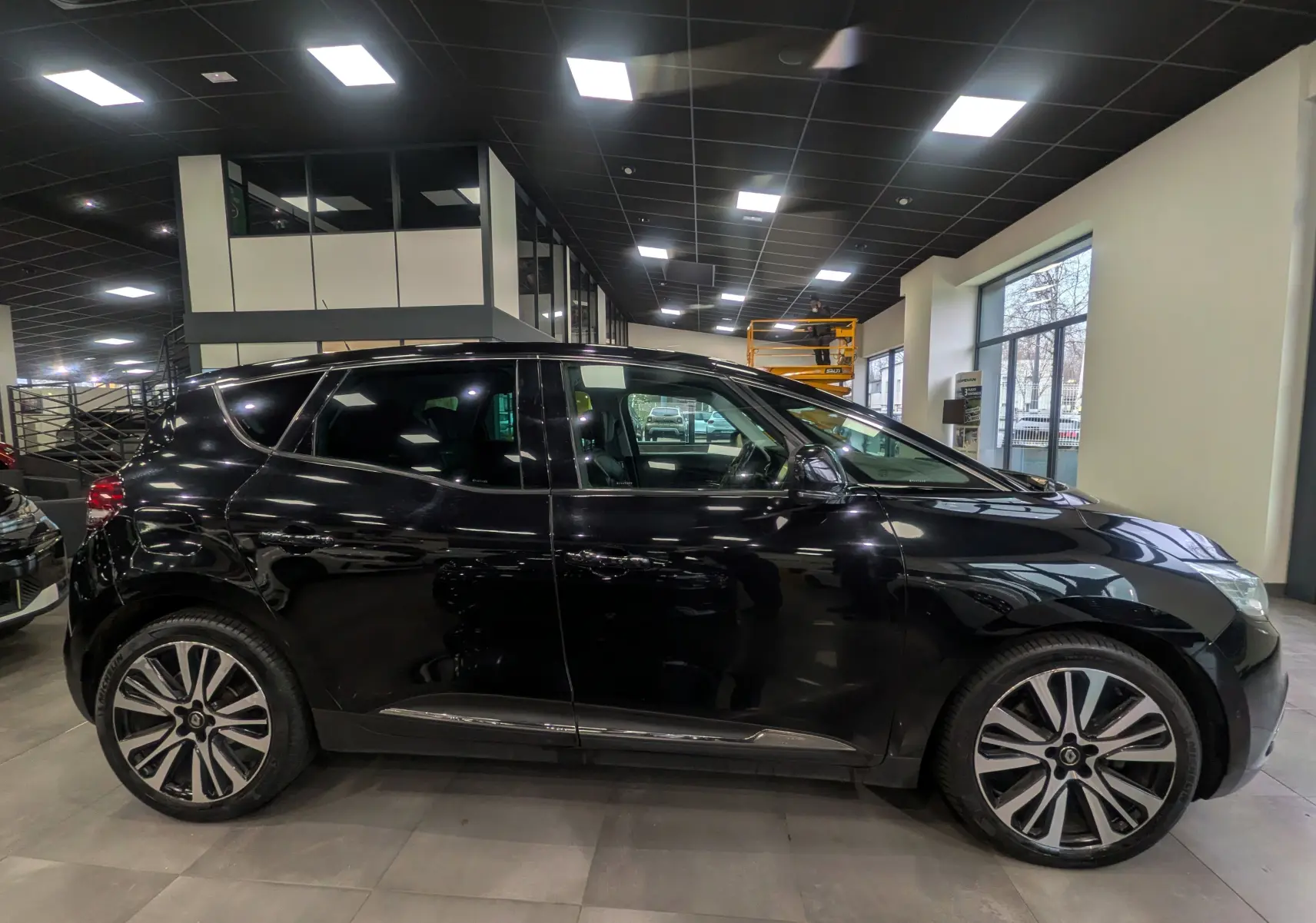 Profil côté gauche de la Renault Scénic IV noir étoilé, avec ses jantes alliage distinctives en intérieur lumineux.