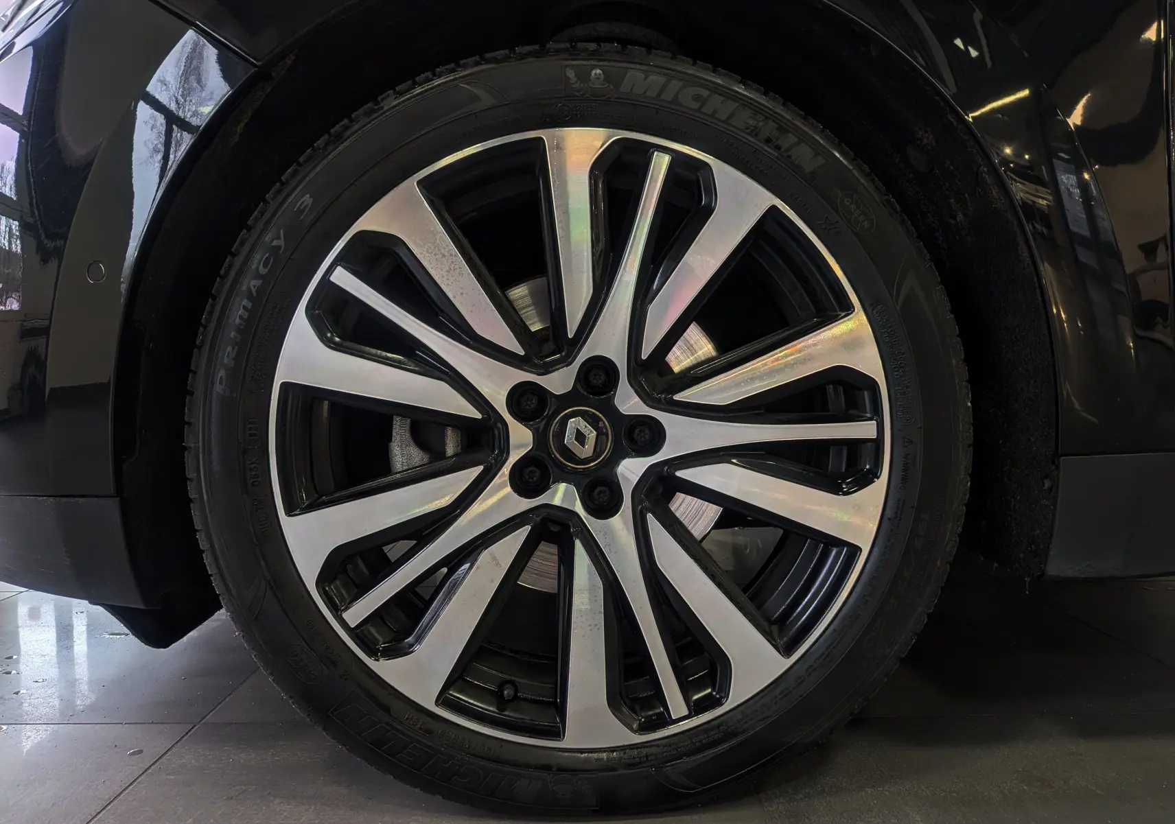 Gros plan sur la jante alliage bicolore du côté avant droit d’un Renault Scénic IV noir étoilé de 2018.