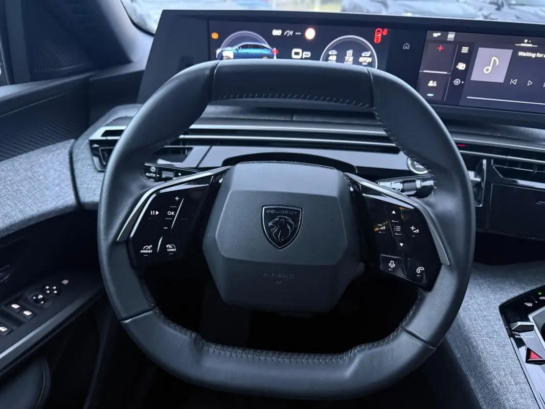 Vue rapprochée du volant cuir noir du Peugeot 3008 Hybrid 145 Allure 2025 avec cockpit numérique en arrière-plan.