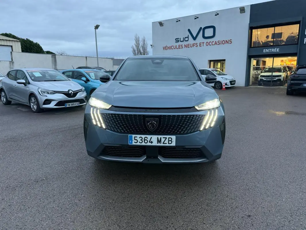 Vue frontale du Peugeot 3008 Hybrid bleu avec feux allumés et calandre distinctive sur parking de concession.