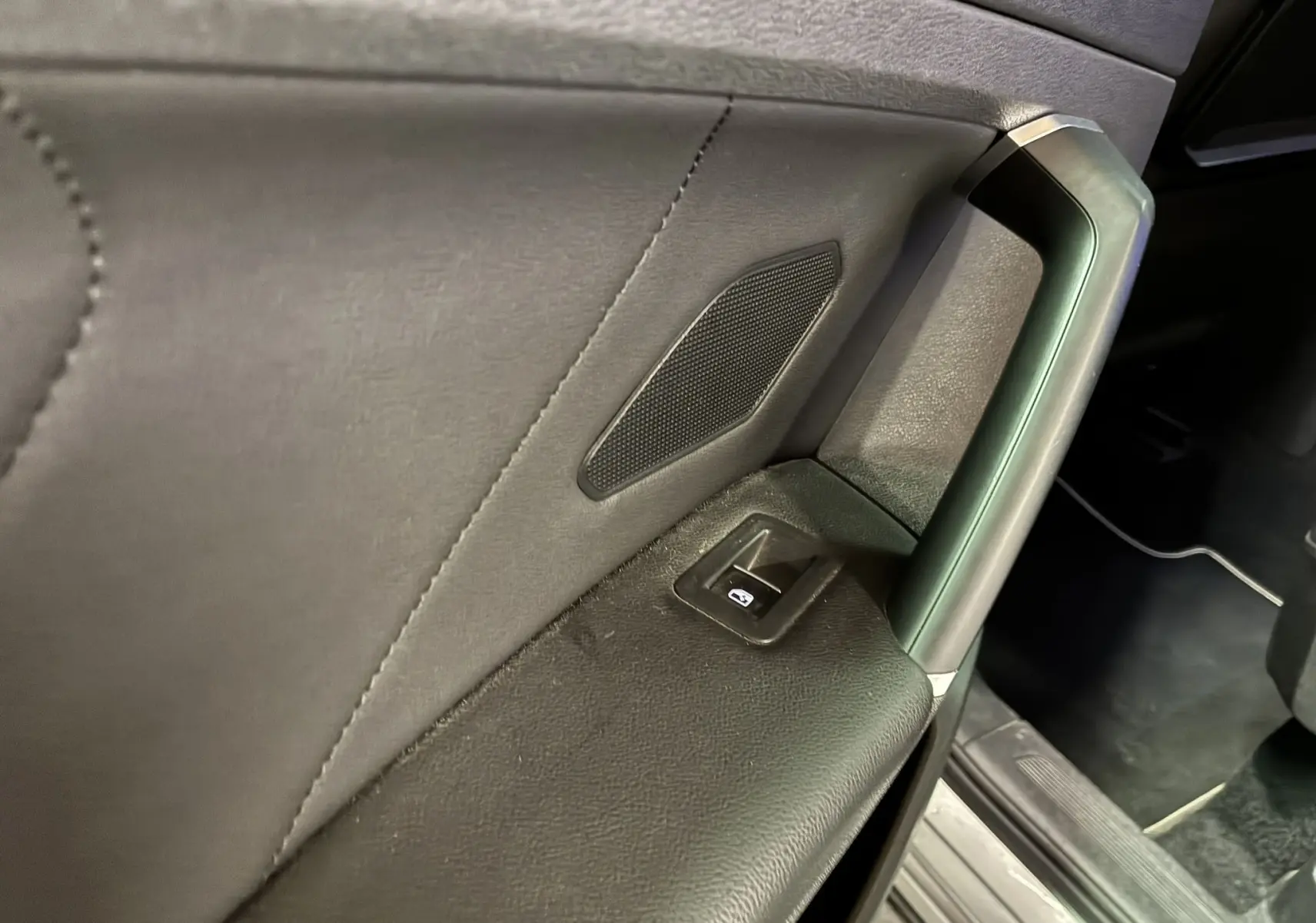 Détail de la porte intérieure côté gauche du Volkswagen Tiguan gris 2017, avec bouton de lève-vitre et haut-parleur intégré.