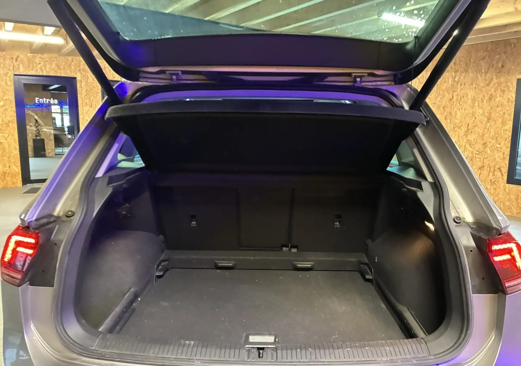 Vue arrière du coffre ouvert d'un Volkswagen Tiguan gris 2017, mettant en valeur l'espace de chargement et les feux arrière allumés.