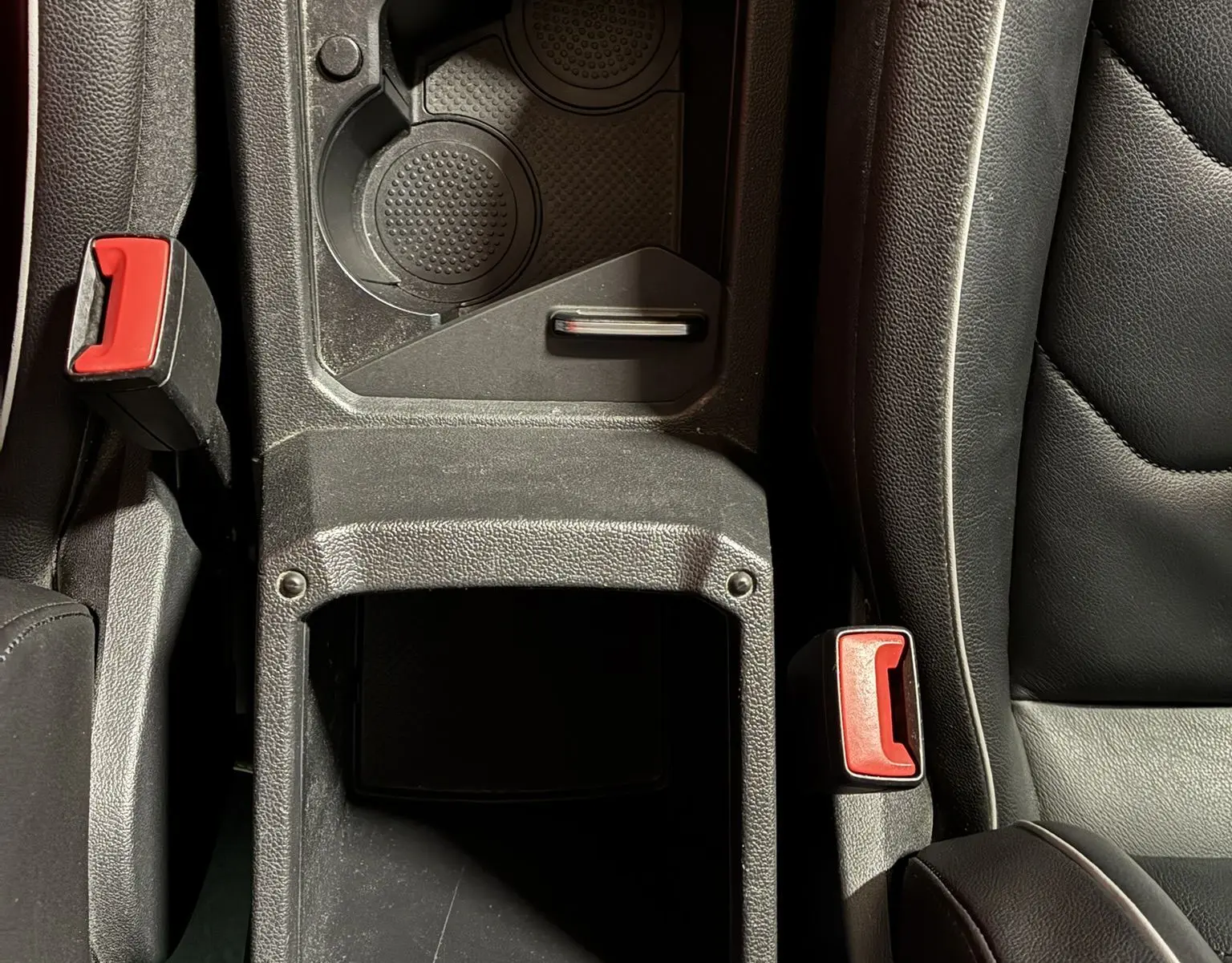 Vue plongeante sur la console centrale noire en cuir du Volkswagen Tiguan 2.0 TDI 150 Carat avec porte-gobelets et ceintures rouges.