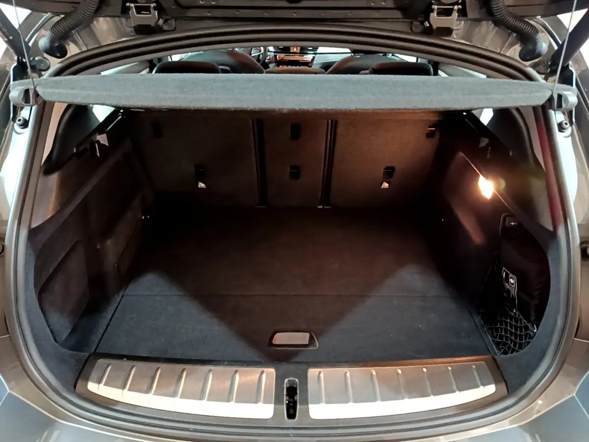 Coffre ouvert vu de l'arrière d'une BMW X2 gris foncé, avec tapis noir et éclairage intérieur à droite.