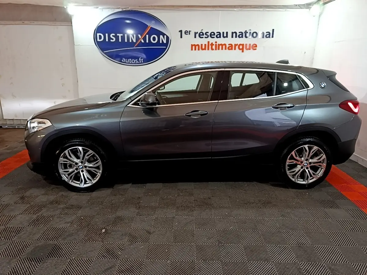BMW X2 sDrive18i Lounge gris foncé vue de profil côté gauche, avec jantes alliage et logo BMW sur l'aile arrière.