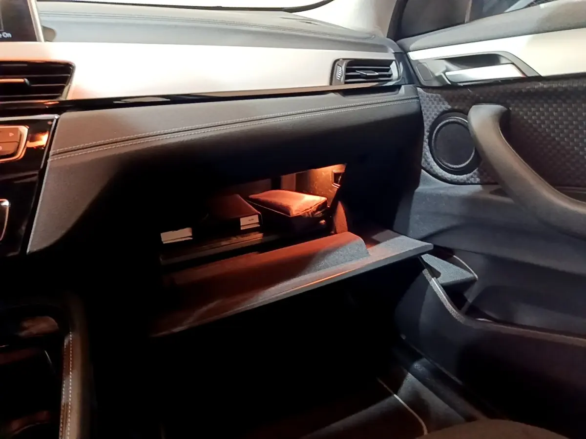 Intérieur BMW X2 sDrive18i 2021, vue côté passager sur boîte à gants ouverte avec éclairage intérieur chaud.