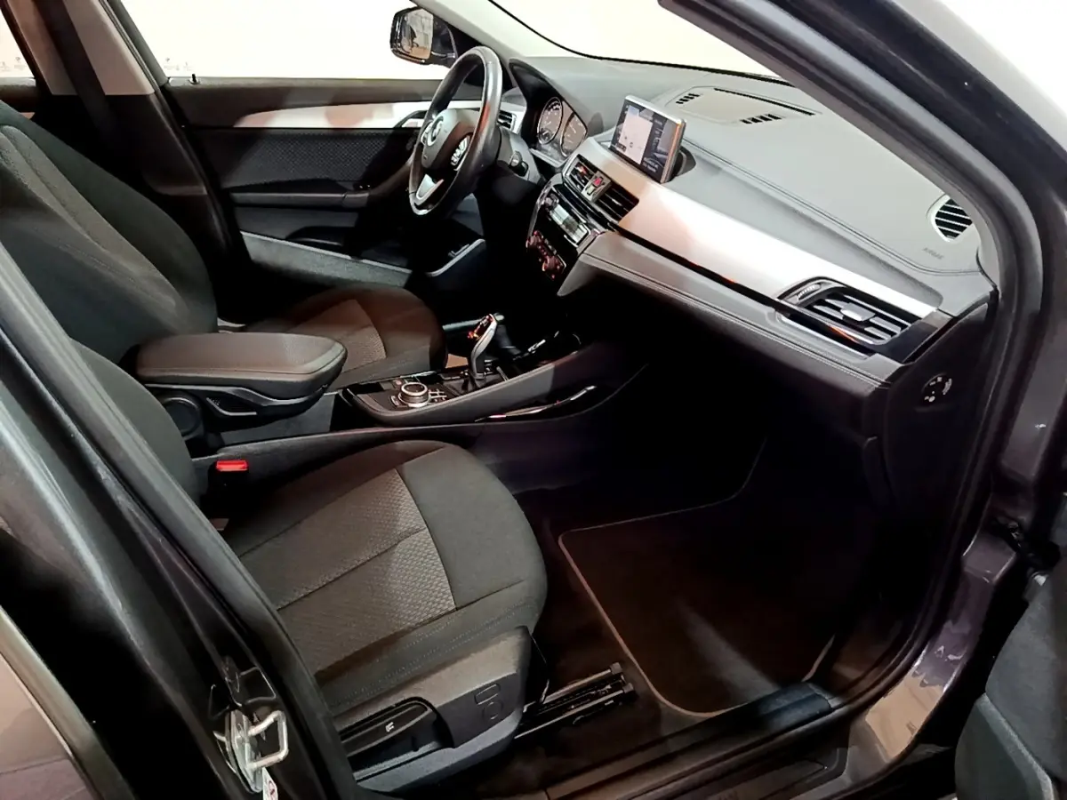 Vue intérieure côté conducteur de la BMW X2 sDrive18i Lounge 2021, avec tableau de bord moderne et sièges gris foncé.