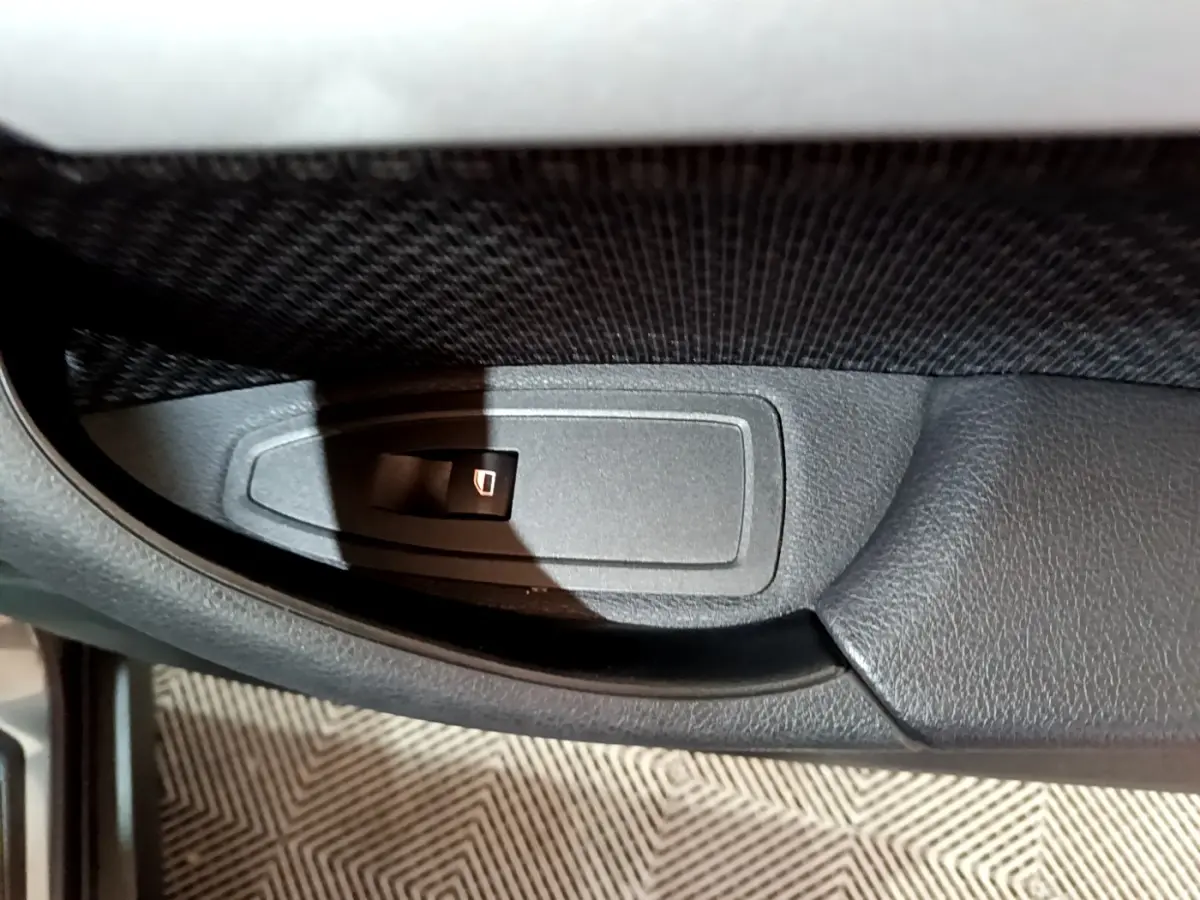 Bouton de commande de lève-vitre sur la porte intérieure côté gauche d'une BMW X2 gris foncé, vue rapprochée.