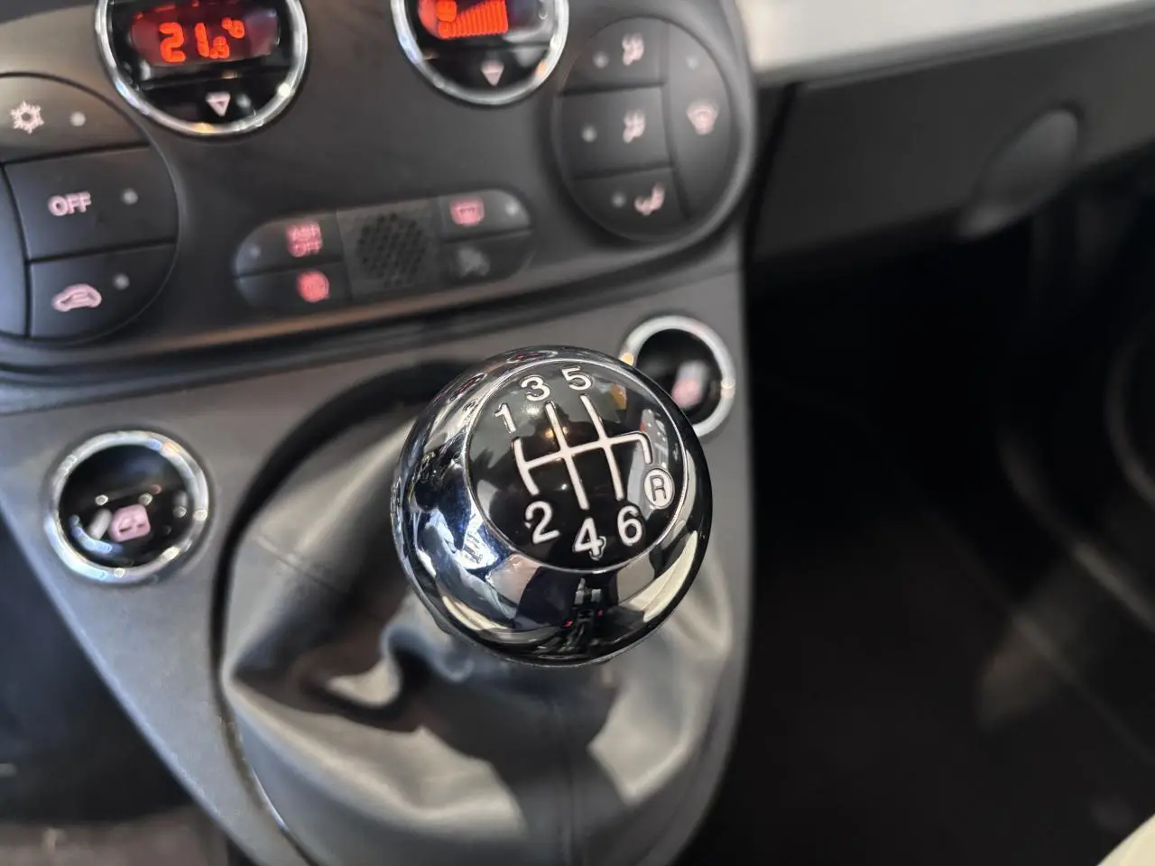 Gros plan sur le levier de vitesses manuel chromé de la Fiat 500 avec tableau de bord noir en arrière-plan.