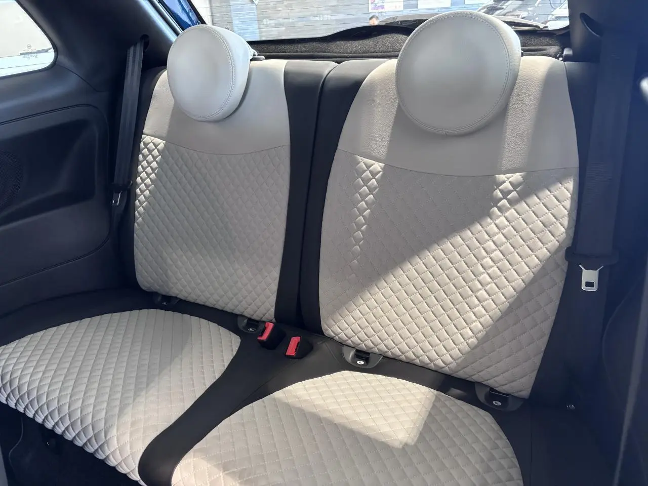 Vue intérieure sur la banquette arrière beige matelassée de la Fiat 500, avec ceintures de sécurité visibles.