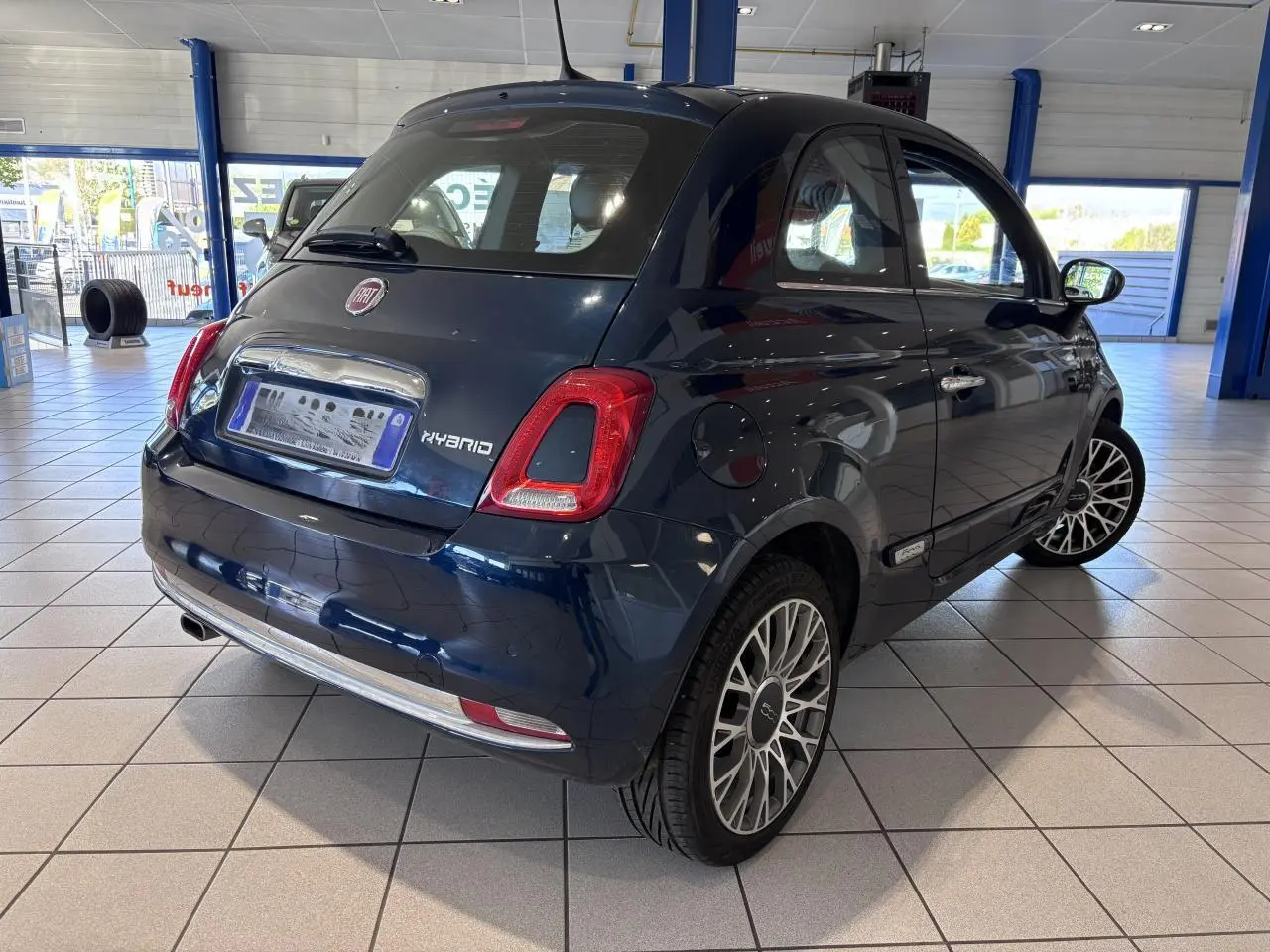 Vue 3/4 arrière droite d'une Fiat 500 hybride bleu foncé avec jantes alliage et détails chromés en showroom.