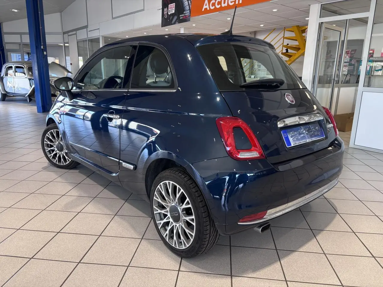 Fiat 500 bleu foncé vue 3/4 arrière droit en intérieur avec jantes alliage et détails chromés.