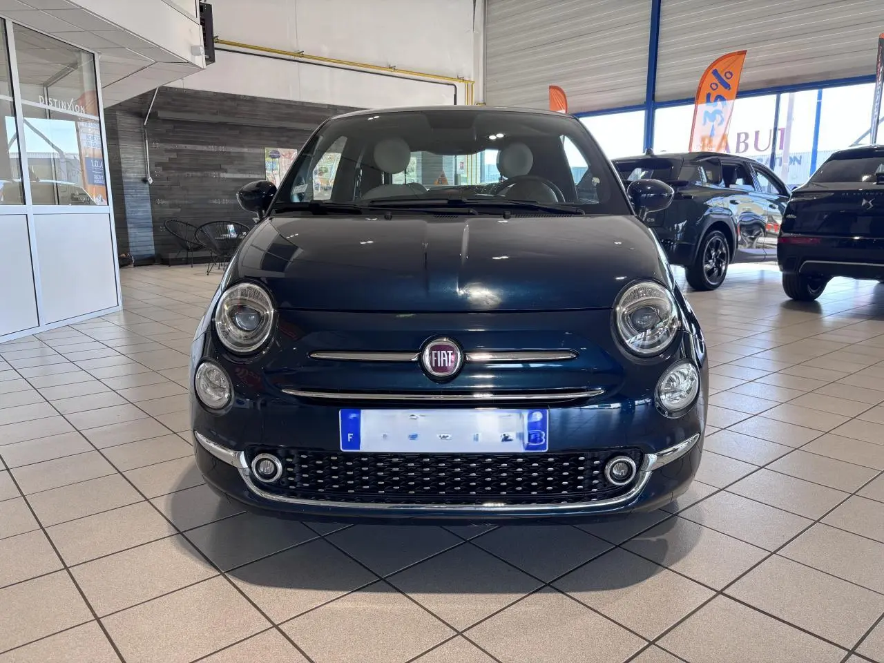 Vue avant d'une Fiat 500 noire en showroom, mettant en valeur sa calandre chromée et ses phares ronds distinctifs.