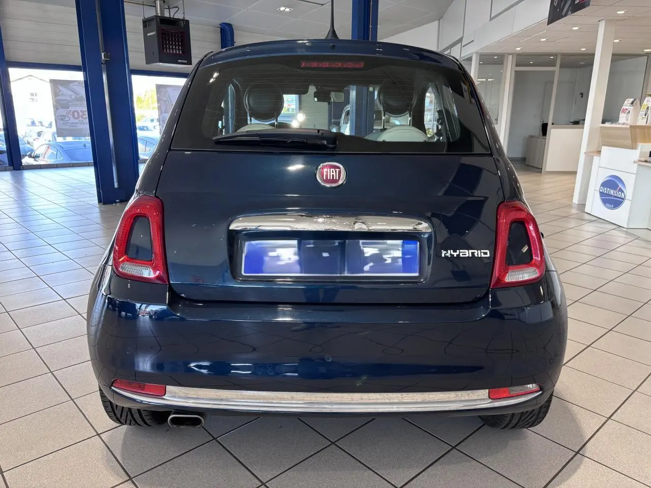 Vue arrière d'une Fiat 500 bleu foncé en showroom, avec logo Fiat et badge Hybrid visibles.