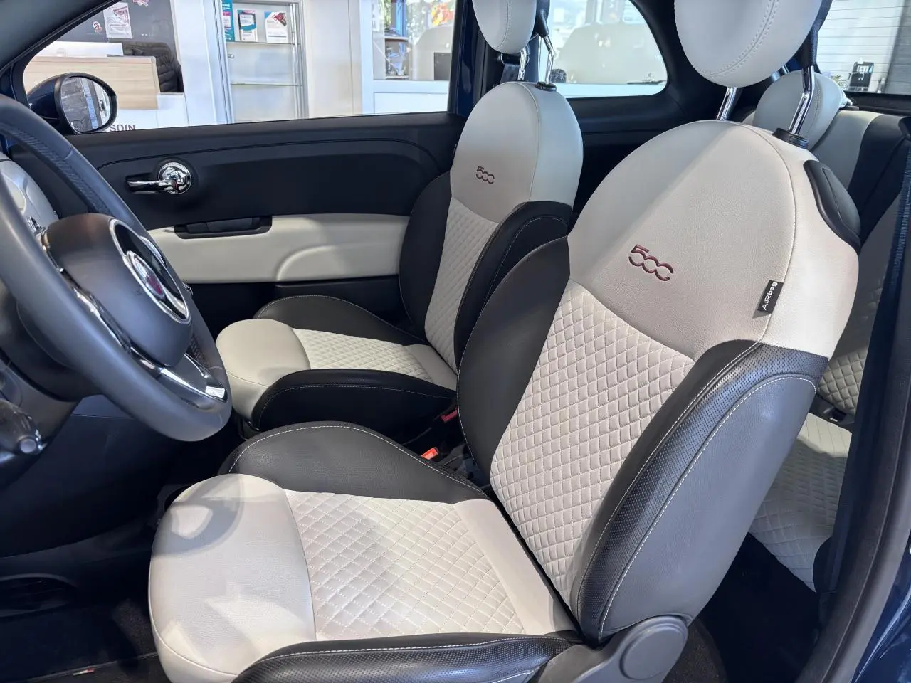 Vue intérieure côté conducteur de la Fiat 500 avec sièges bi-ton beige et noir matelassés et logo 500 brodé.