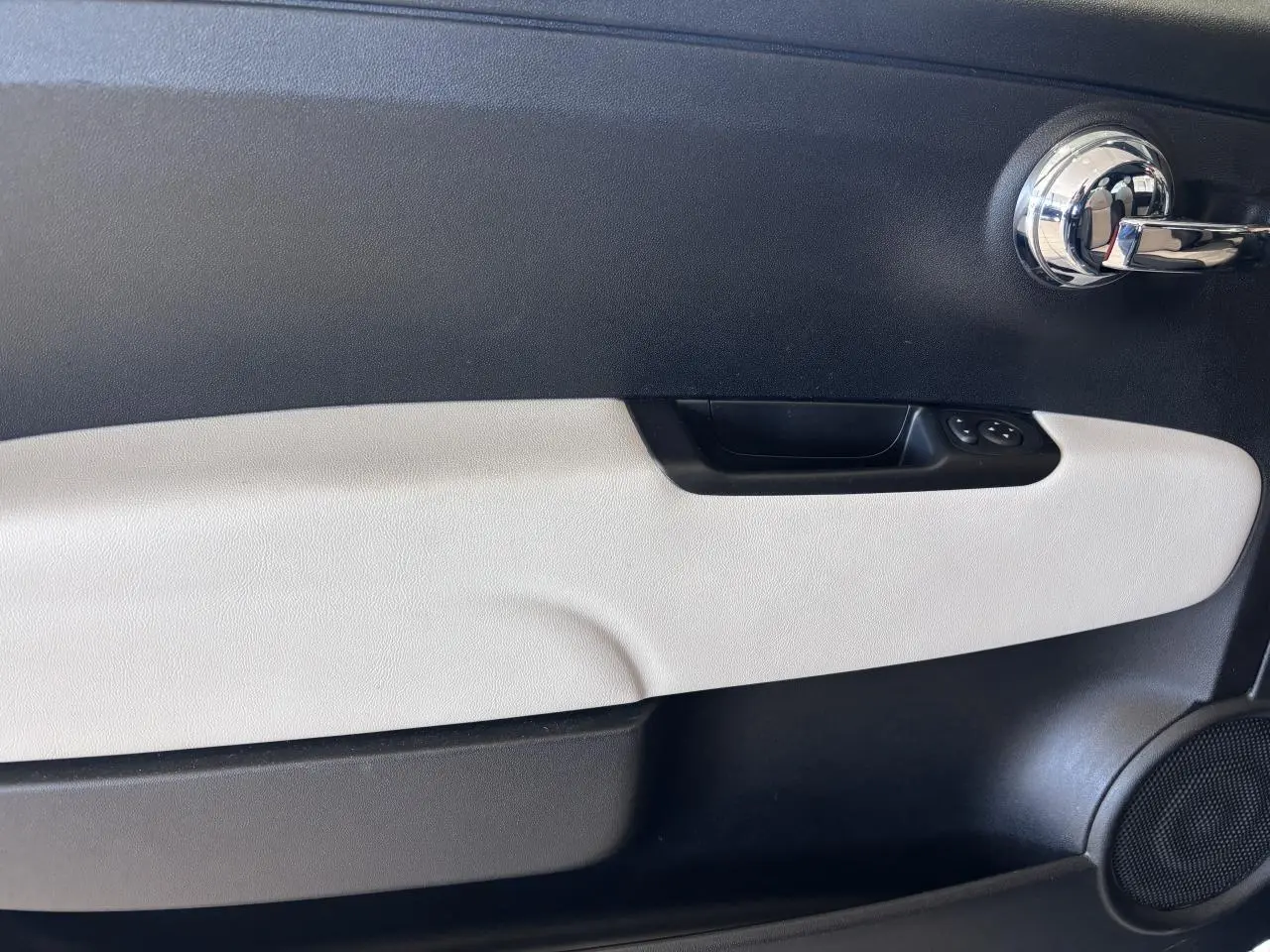 Gros plan sur la porte intérieure côté gauche de la Fiat 500 verte, avec poignée chromée et panneau bicolore noir et beige.