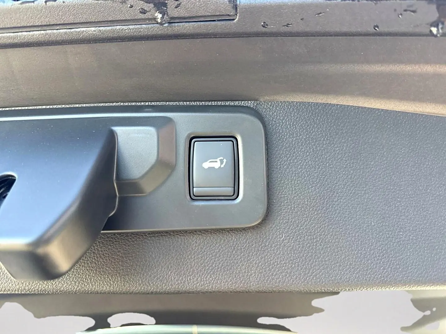 Gros plan sur le bouton d'ouverture électrique du coffre, intérieur noir texturé du Renault Symbioz gris rafale.