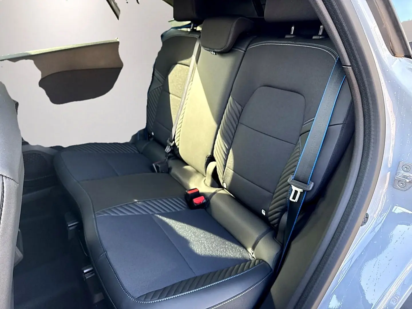 Vue intérieure sur la banquette arrière noire avec surpiqûres bleues du Renault Symbioz gris rafale, porte ouverte côté droit.