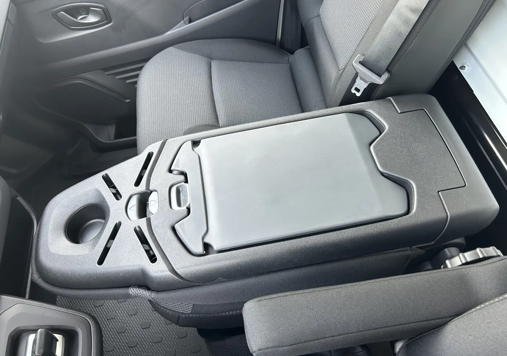 Vue rapprochée de la console centrale noire et des sièges tissu gris du Renault Trafic Fourgon blanc côté passager.